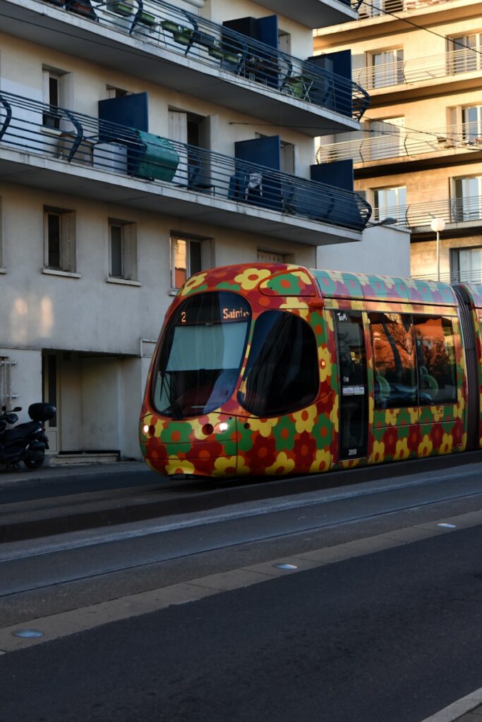 A colorful train traveling down a street next to tall buildings