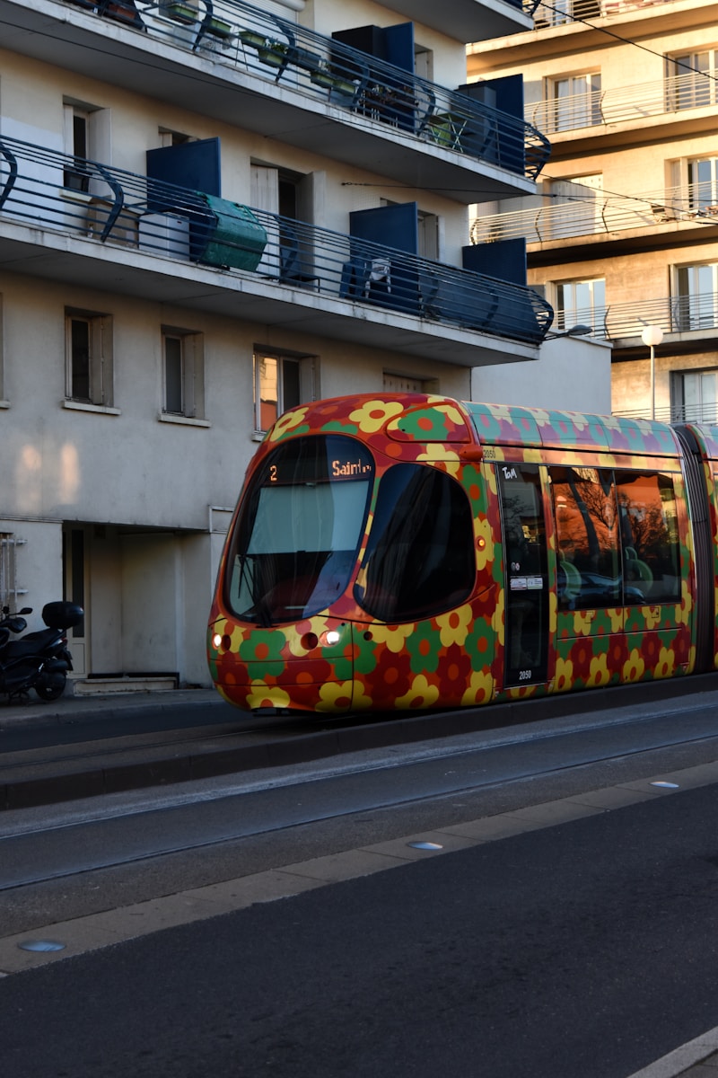 A colorful train traveling down a street next to tall buildings