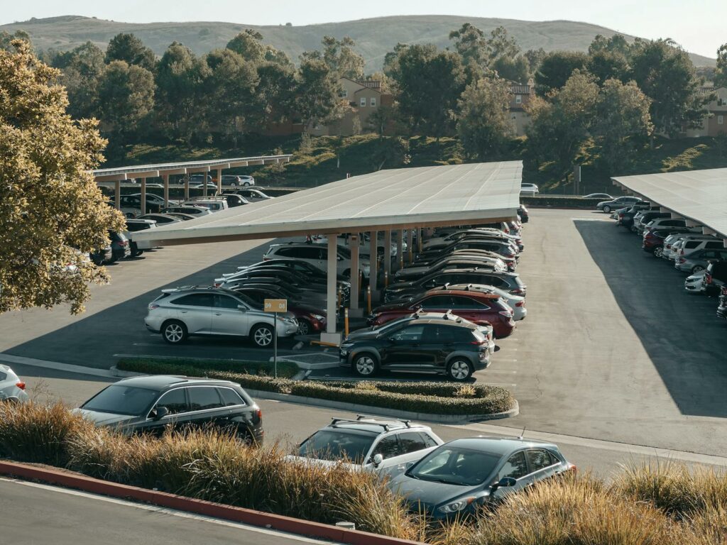 View of a large parking lot with solar panel shades and diverse vehicles parked.